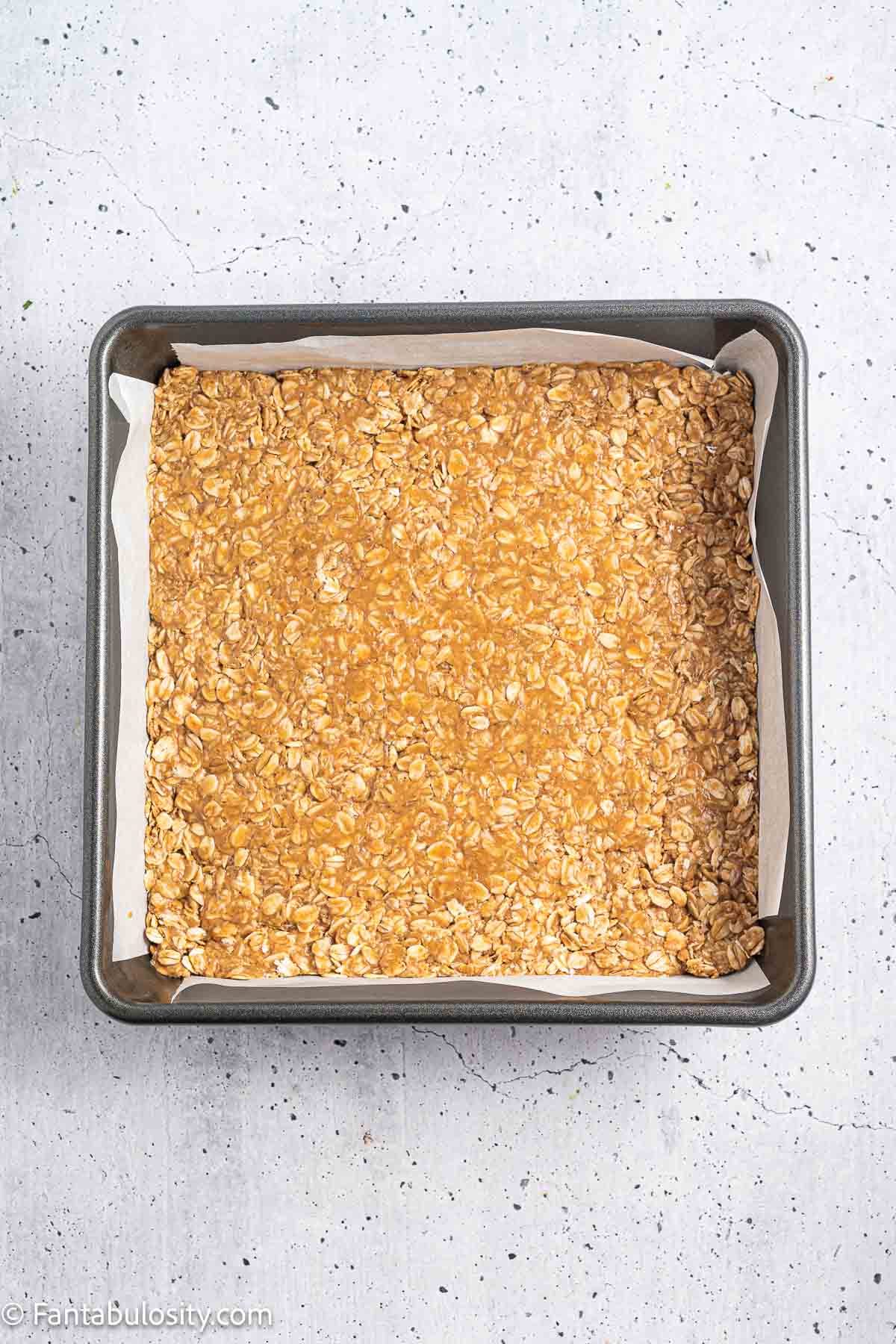 Peanut butter and oat mixture pressed evenly into a parchment-lined square pan.