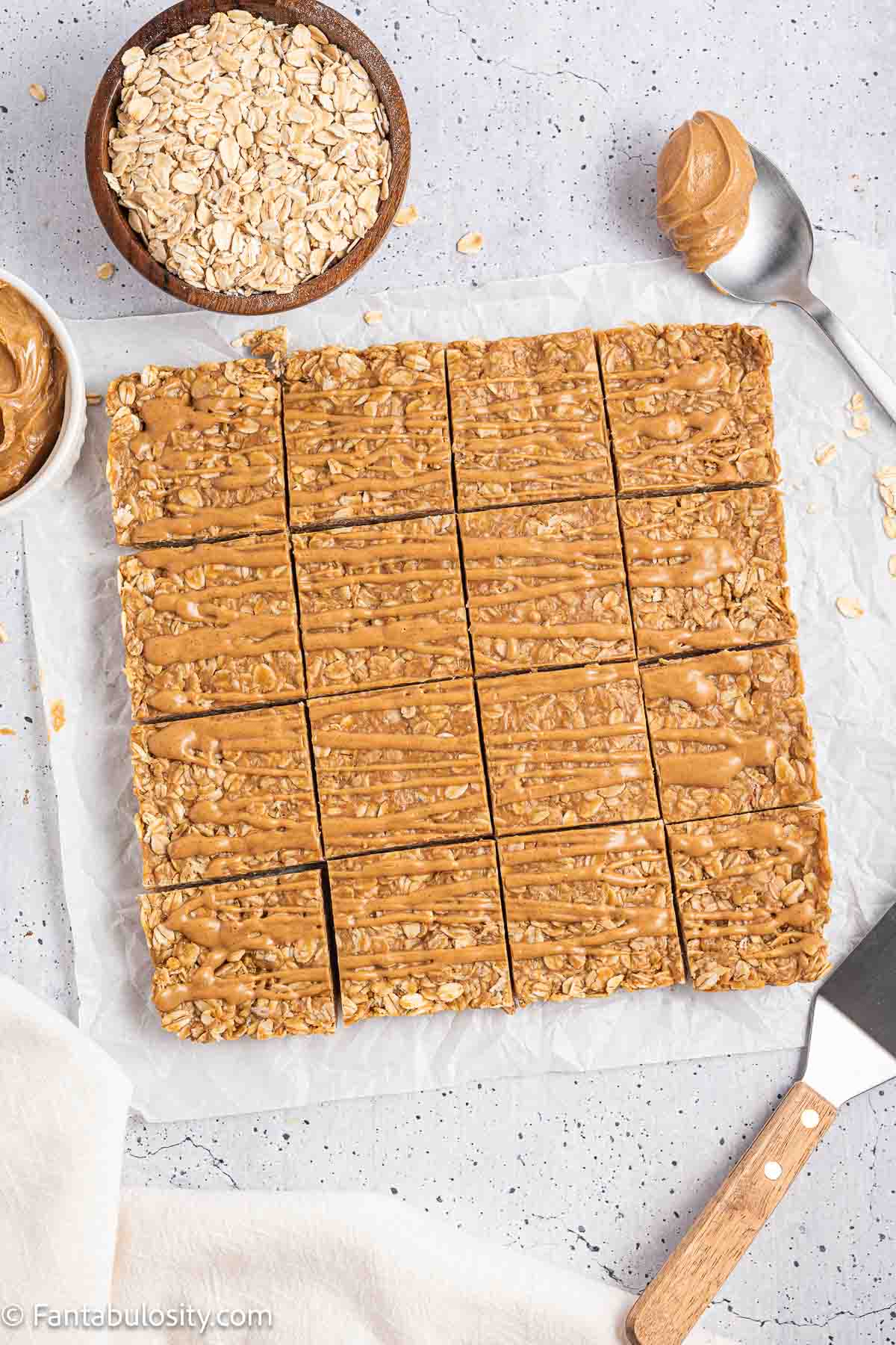 A slab of peanut butter oatmeal bars cut into 16 squares on parchment paper.