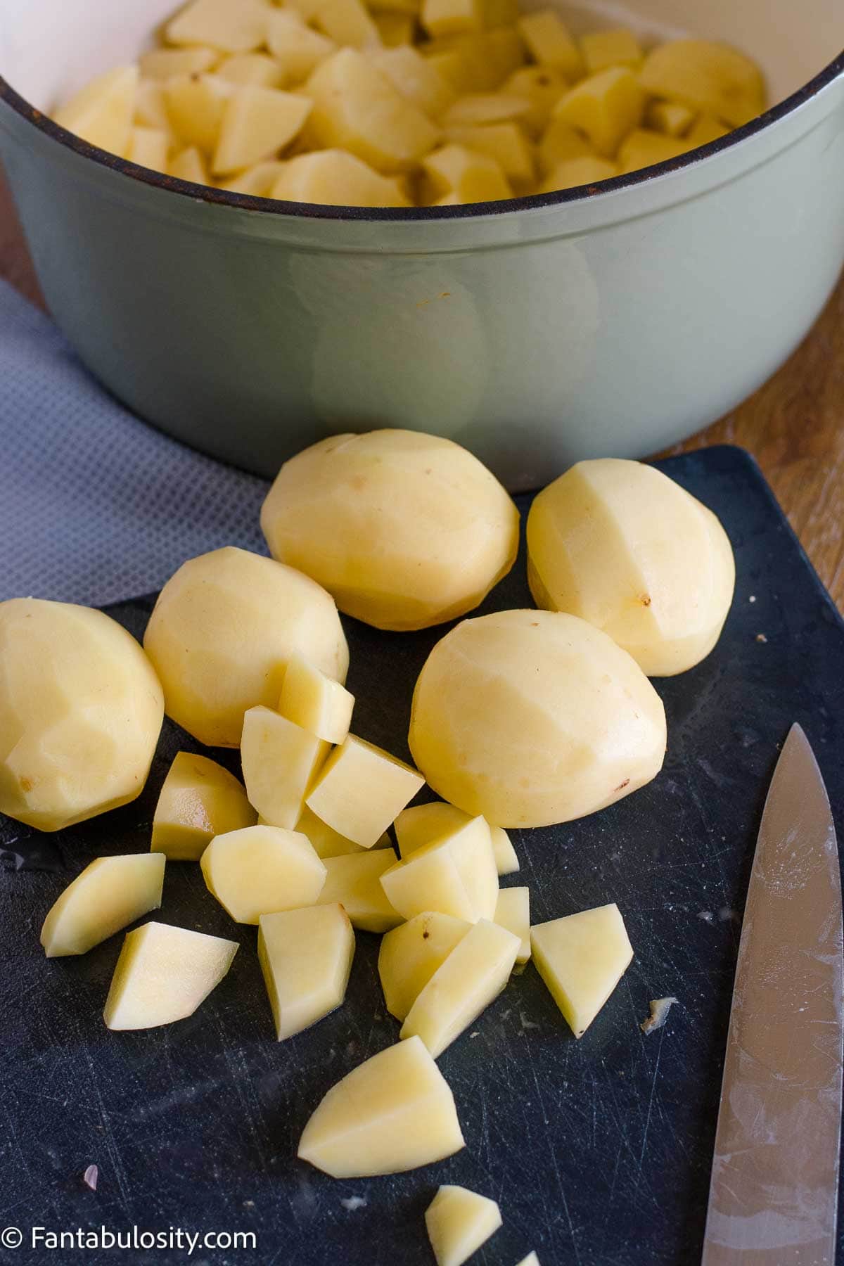 Peeled Yukon Gold potatoes cut into chunks beside a pot.