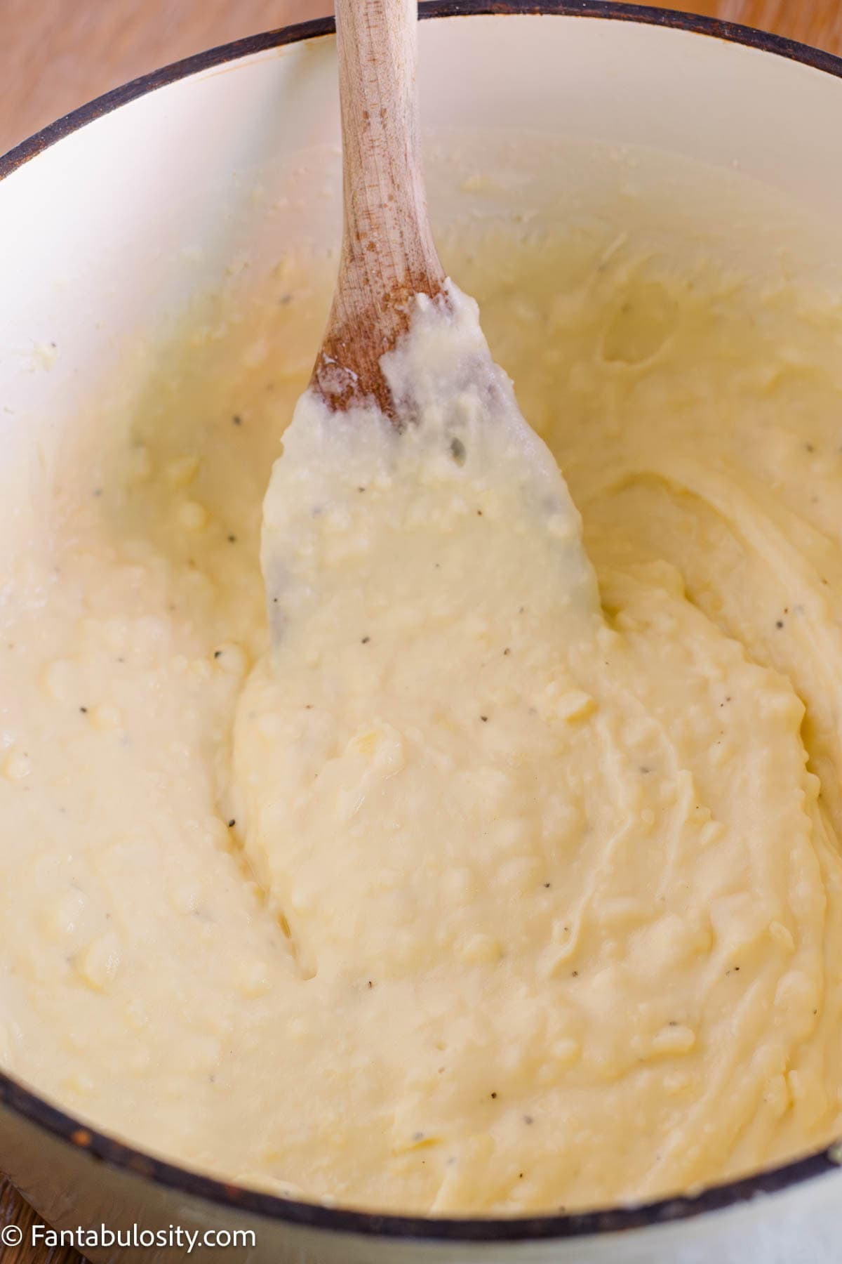 Creamy mashed potatoes being gently stirred with a wooden spoon.