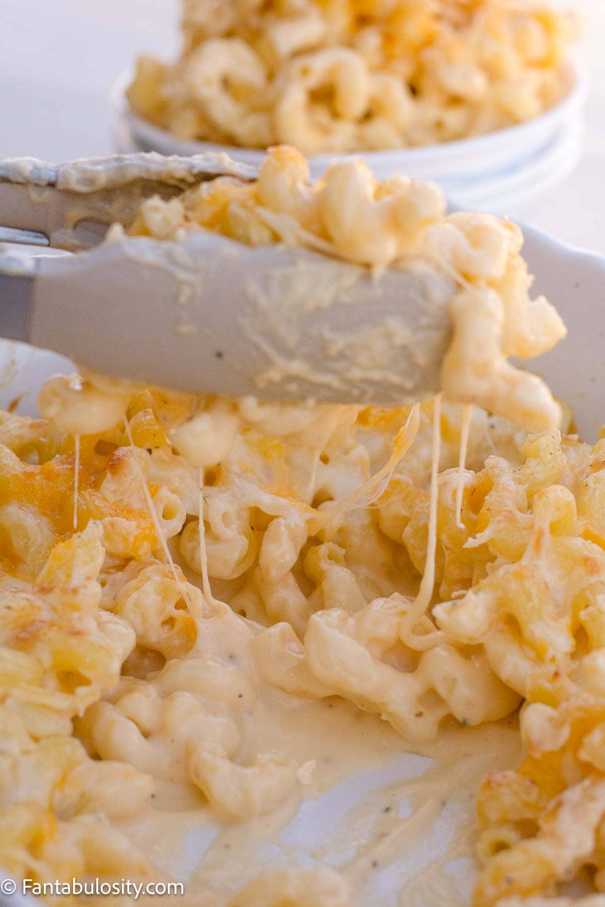 Melted cheese stretching from cavatappi lifted out of the baking dish.