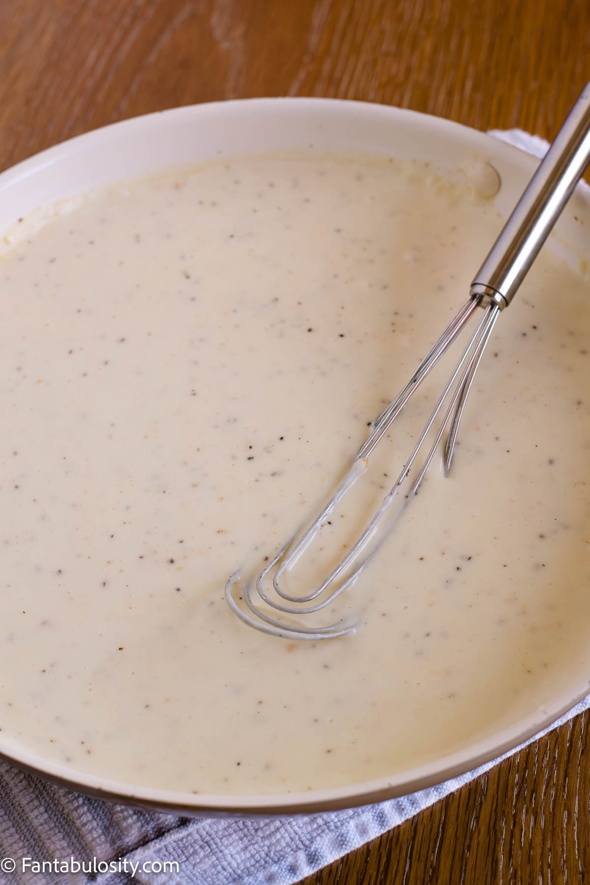 Seasoned milk sauce in a skillet with a whisk.